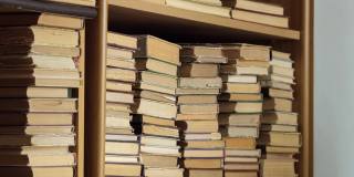书架上有旧书。一位女士正在图书馆的书架上找书。人类选择书籍。白种人用手触摸书架上的书。阅读与教育的概念