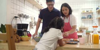 一对亚洲夫妇带着可爱的小女儿一起在厨房准备早餐