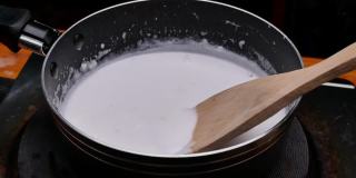 用手在锅中慢慢搅拌椰奶，准备泰国甜点。