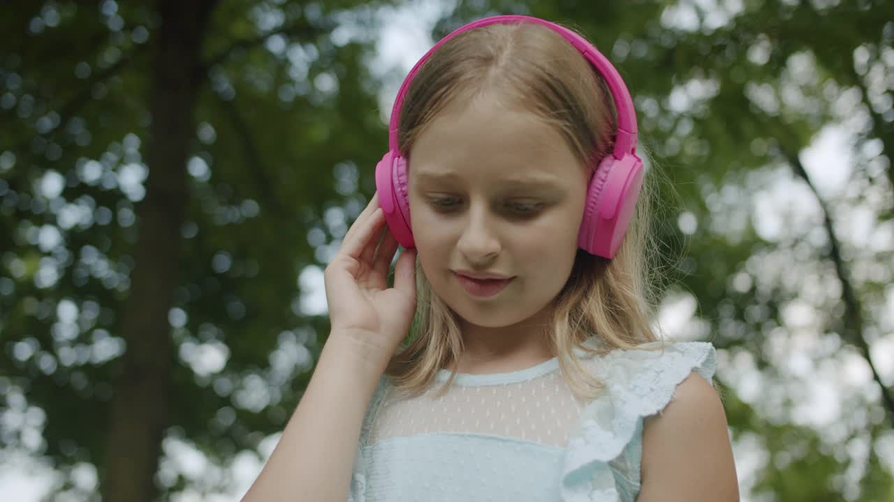 小孩子在公园里戴着时髦的粉色耳机听音乐，然后往下看