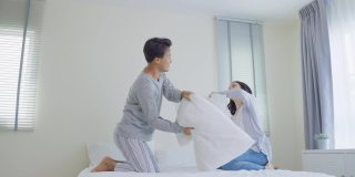 亚洲年轻美丽的情侣在床上一起枕头大战。有吸引力的新婚男女感到幸福，享受清晨在卧室里玩耍的活动。家庭关系。