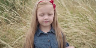 害羞迷人的高加索小女孩在秋天的户外田野里摆姿势。美丽可爱的孩子的肖像看着相机微笑调整长长的金发。自然和童年的概念。