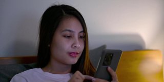 孤独的年轻亚洲女人使用智能手机和社交媒体盖着毯子在卧室