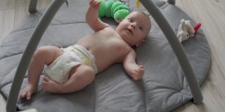 可爱的3个月的小男孩学习从他的背部到腹部，当他躺在游戏垫上，婴儿活动在婴儿游乐场的软垫上。