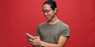 开朗的亚洲男人穿着t恤戴着眼镜在智能手机上写信息