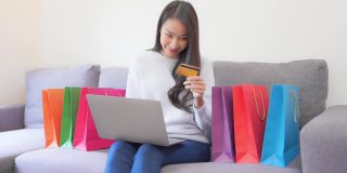 年轻的亚洲女性使用笔记本电脑或手机和信用卡在网上购物