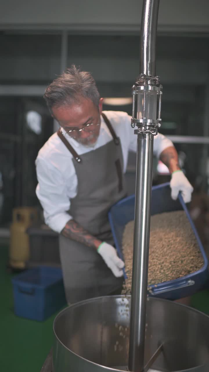 亚洲华人高级男工人装载生咖啡豆，为咖啡烘焙过程做准备