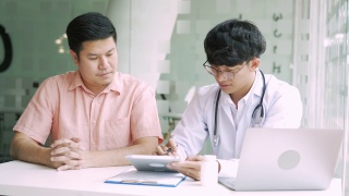 亚洲医生在诊所边用药片边和病人交谈，解释病人的病情和治疗结果。视频素材模板下载