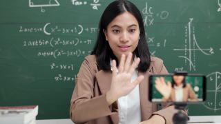 年轻的亚洲女教师坐在和学生视频会议。女教师在课堂上通过智能手机在线课程直播培训数学。视频素材模板下载