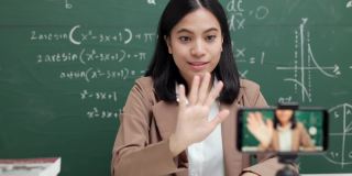 年轻的亚洲女教师坐在和学生视频会议。女教师在课堂上通过智能手机在线课程直播培训数学。