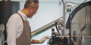亚裔华裔高级技工操作咖啡烘焙机的控制面板触摸屏，为咖啡烘焙过程做准备