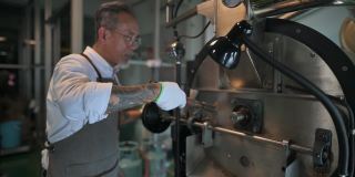 亚洲华人高级技工微笑着拿着特里尔从咖啡烘焙机中提取咖啡豆烘焙生咖啡豆闻检查
