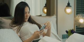 亚洲女性早上躺在床上用智能手机查看社交应用。