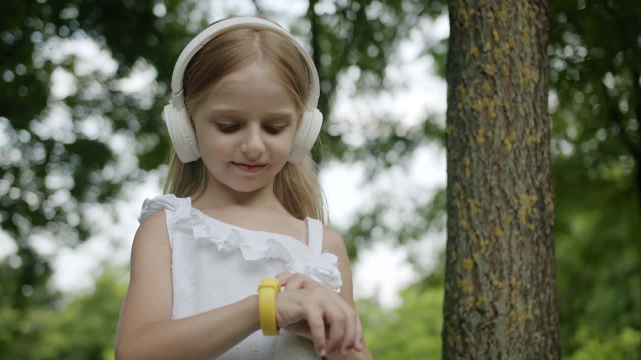 快乐的孩子使用现代数字小玩意智能手表和白色耳机