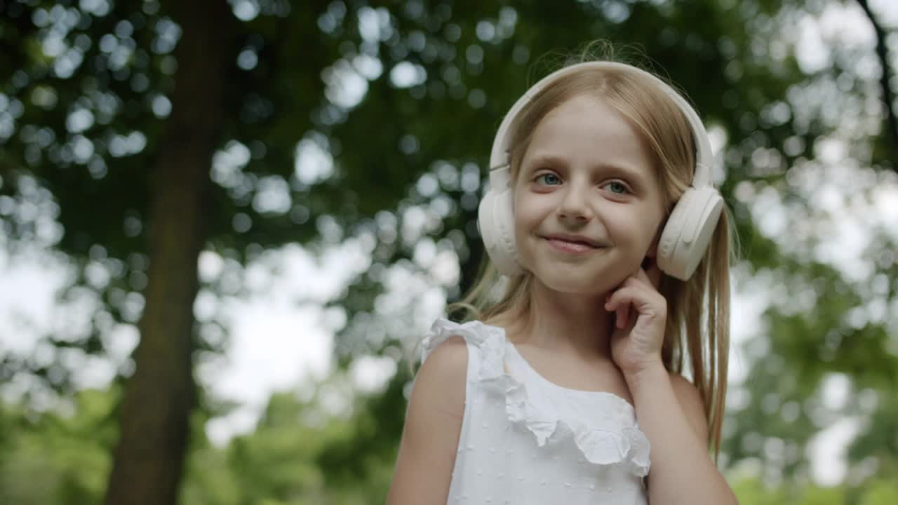 快乐的孩子在公园里用现代的白色耳机听音乐，向上看