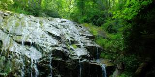 水流在巨大的岩石表面上，瀑布上方有美丽的绿色灯光。格伦伯尼瀑布附近吹岩石，北卡罗莱纳，美国。