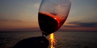 酒杯里的酒映衬着海面上的夕阳。缓慢的运动。