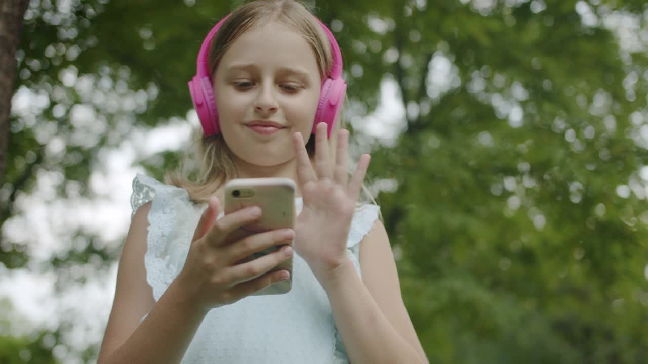 快乐少年在线视频通话与现代粉红色耳机在公园