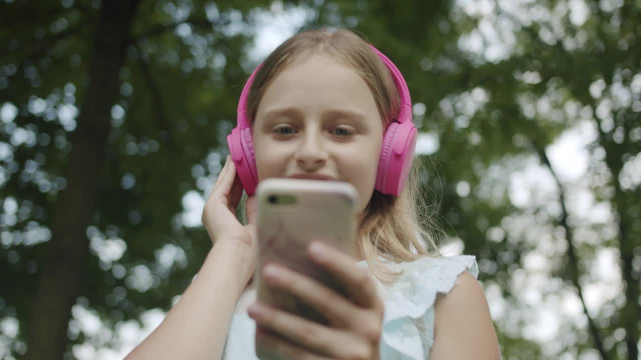 快乐的少年听音乐现代粉红色耳机和手机