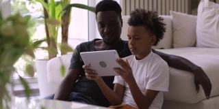 十几岁的非洲男孩在平板电脑Spbi上播放爸爸的电影。一家人一起看视频。享受