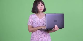 工作室拍摄美丽的亚洲孕妇使用笔记本电脑在绿色的工作室背景