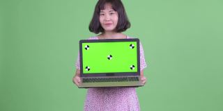 工作室拍摄的美丽怀孕的亚洲女人显示拷贝空间从笔记本电脑在绿色的工作室背景