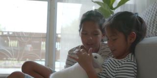 两个亚洲女孩兄弟姐妹抱着他们的宠物兔子一起在客厅里充满爱地玩耍。