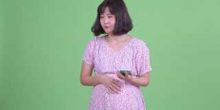 工作室拍摄的美丽怀孕的亚洲妇女在电话交谈在绿色工作室的背景
