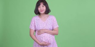 工作室拍摄的美丽怀孕的亚洲妇女在绿色的工作室背景