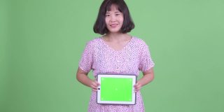 摄影棚拍摄的美丽怀孕的亚洲妇女手持数字平板电脑与复制空间在绿色的摄影棚背景