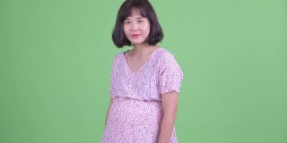 摄影棚拍摄的美丽的怀孕亚洲妇女微笑和指向相机在绿色的摄影棚背景