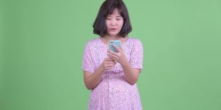 工作室拍摄美丽的亚洲孕妇使用手机和得到好消息在绿色工作室背景
