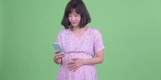 摄影棚拍摄美丽的怀孕亚洲妇女微笑和使用手机在绿色的摄影棚背景