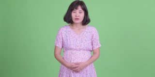 摄影棚拍摄美丽的怀孕亚洲妇女看起来无聊的绿色摄影棚背景