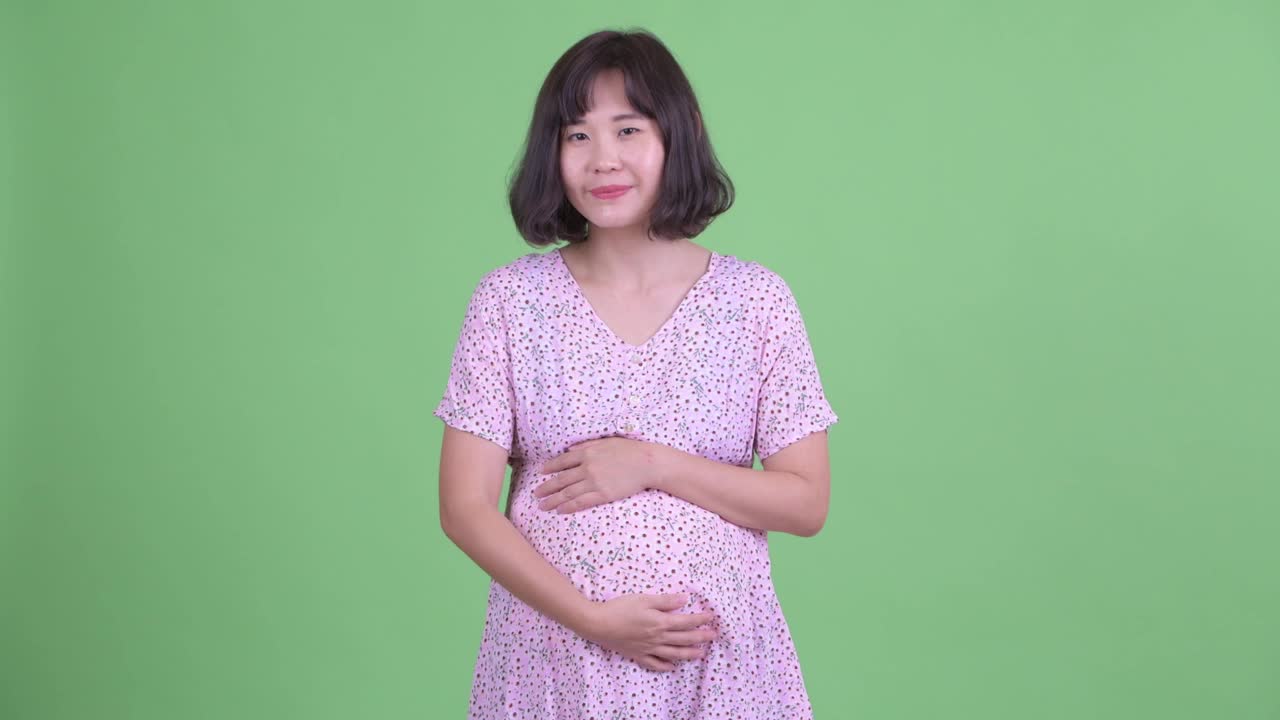 摄影棚拍摄了美丽的亚洲孕妇说话和抱着肚子在绿色的摄影棚背景