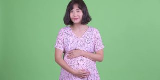 摄影棚拍摄了美丽的亚洲孕妇说话和抱着肚子在绿色的摄影棚背景