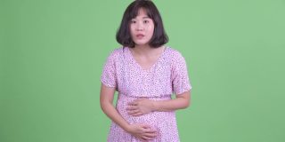摄影棚拍摄的美丽的怀孕亚洲妇女看起来高兴惊讶的绿色摄影棚背景