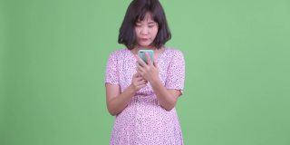 工作室拍摄美丽的怀孕亚洲妇女使用手机和得到坏消息在绿色工作室背景