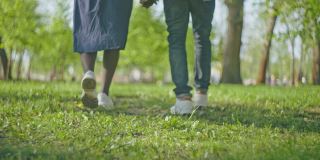 情侣在夏日公园散步，手牵手，脚特写，慢动作