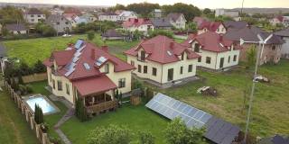 鸟瞰图的郊区住宅和私人住宅与绿草覆盖的院子，太阳能电池板的屋顶，游泳池与蓝色的水和风力发电机。
