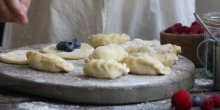 一位妇女用面粉在木制背景上自制了一个饺子或Pierogi。传统的乌克兰或波兰食物。