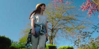 戴着草帽的漂亮女人微笑着站在一棵樱花树下等待。英雄的观点。底部视图。背景是天空和一棵盛开的樱桃树