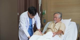 一位年轻的亚洲医生在医院医务室的病床上检查这位老人手术后的膝盖和腿。