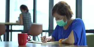 亚洲女雇员戴着口罩在商业办公室工作，与同事保持社交距离，保护冠状病毒或covid-19爆发大流行。职场新常态政策