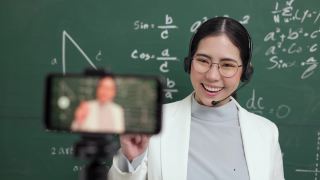 年轻的亚洲女教师站在摄像机和学生视频会议。女教师在课堂上通过智能手机在线课程直播培训数学。视频素材模板下载
