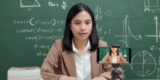 年轻的亚洲女教师坐在和学生视频会议。女教师在课堂上通过智能手机在线课程直播培训数学。