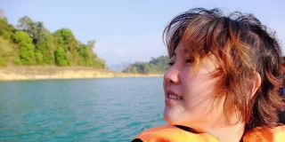 慢镜头，幸福年轻的亚洲女子穿着救生衣微笑着在长尾船上放松清新的风自然“周兰湖(拉恰帕坝)”泰国苏拉塔尼考索国家公园。