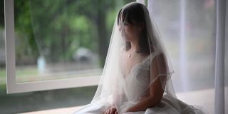 美丽的亚洲中国新娘，戴着面纱，在婚礼当天微笑着在窗口等待她的新郎