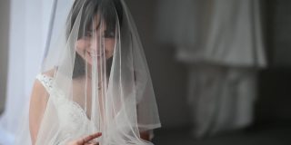 美丽的亚洲华人新娘拉起面纱，微笑着等待新郎在婚礼当天