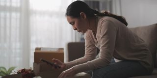 亚洲女人消费者觉得坐沙发不好，拿着电话与网店网上关于在家里订购的问题产品，抱怨